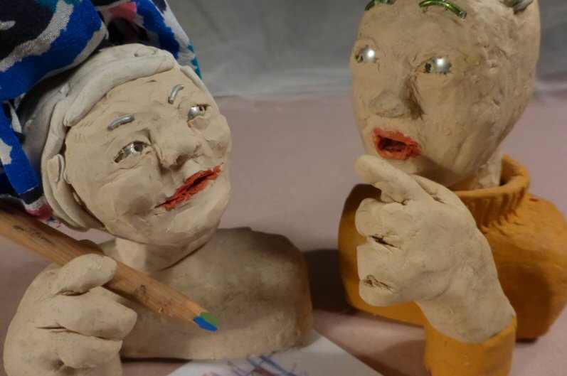 2 plasticine heads with one holding a pencil